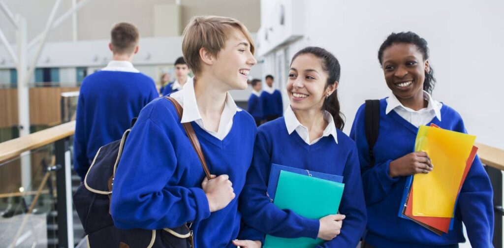 Smiling female students wearing school uniforms walking through school corridor