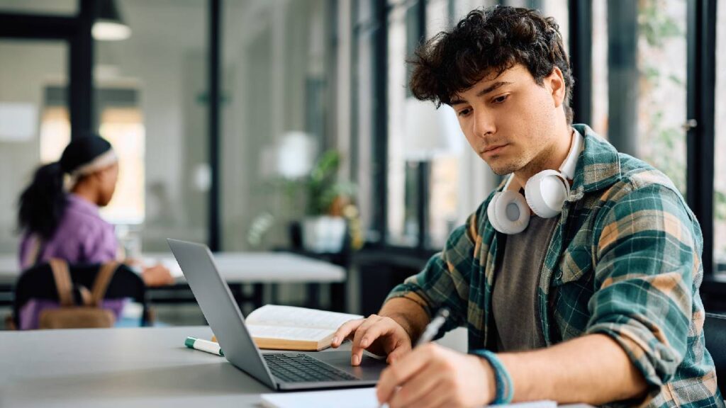 Young student taking notes while e-learning on laptop at the university for his iQTS